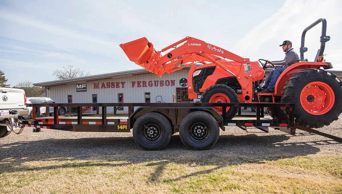 a man is driving a kubota tractor on a 14PI tube top utility trailer