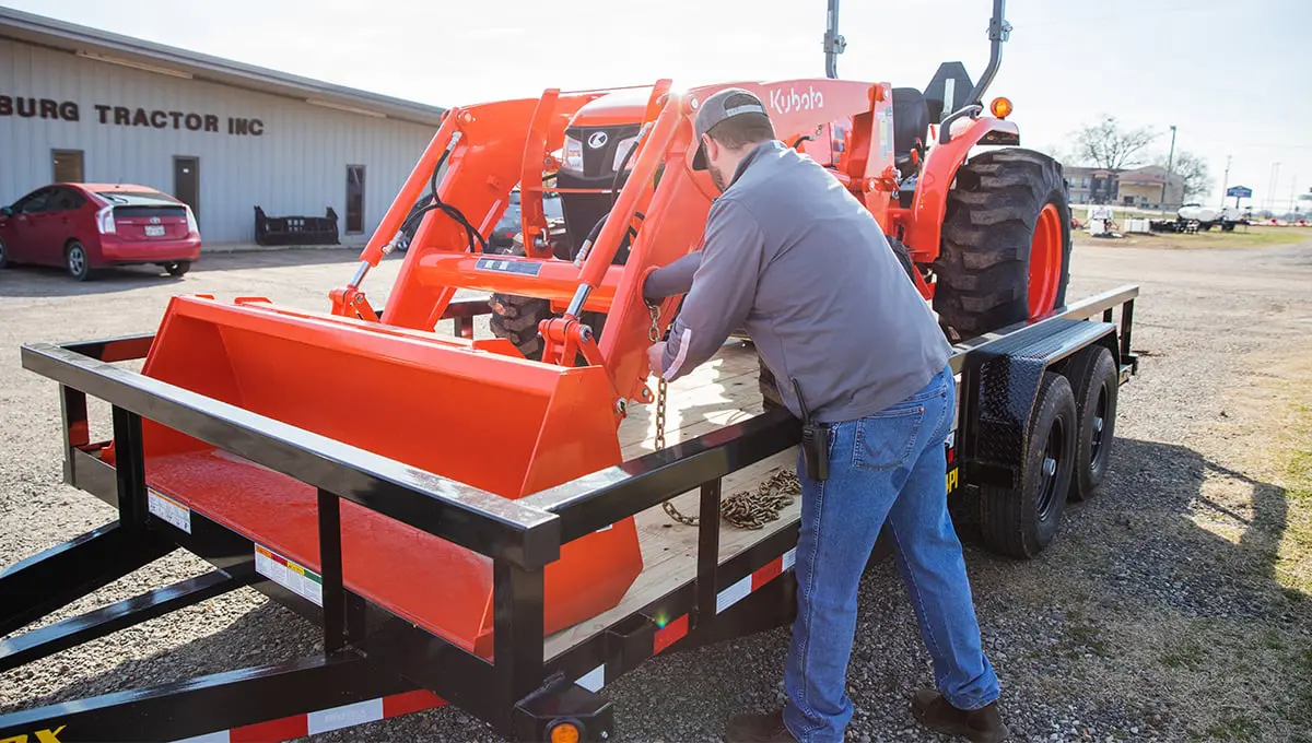 a man loading a kubota tractor on a 14pi utility trailer