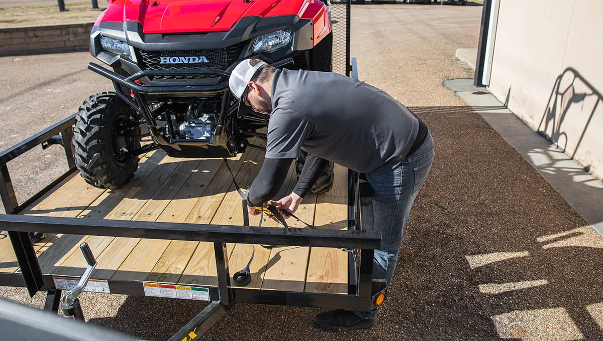 a man is working on a honda atv on a 35sa utility trailer