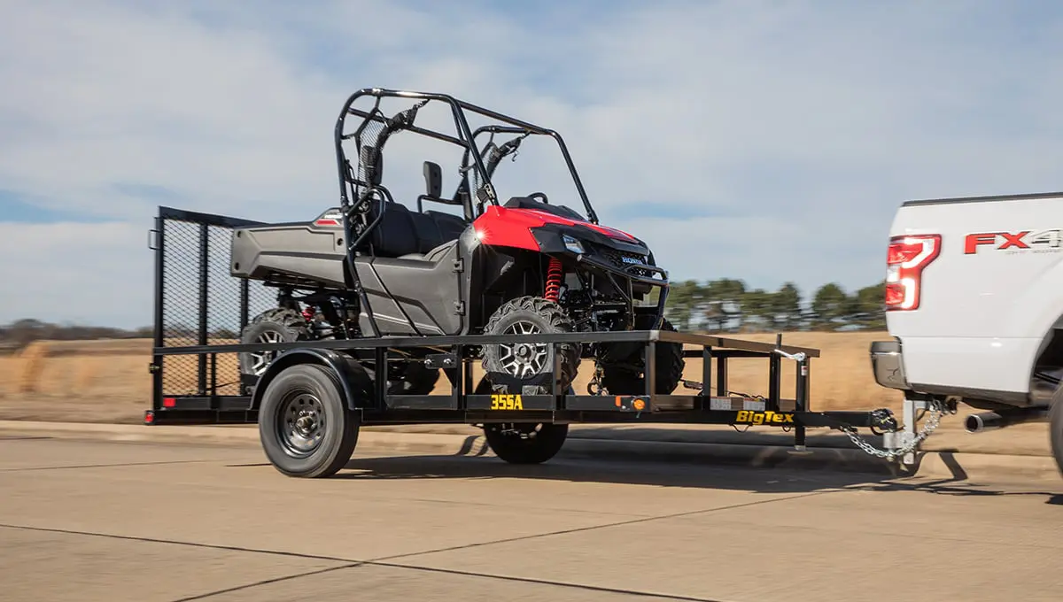 a white truck is towing a 35sa utility trailer with a red atv on it