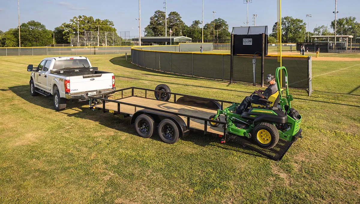 a man is driving a john deere lawn mower on a 60pi trailer