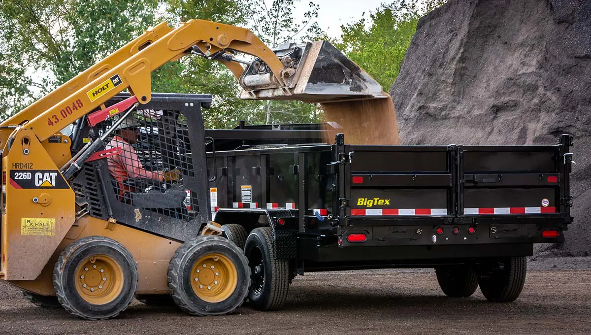 a cat skid steer is loading dirt into a big tex dump trailer