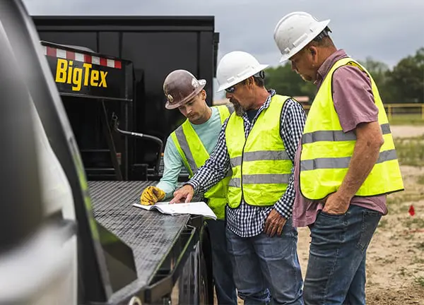 Men Wearing Construction Hats and Vests in Front of a Big Tex Trailer