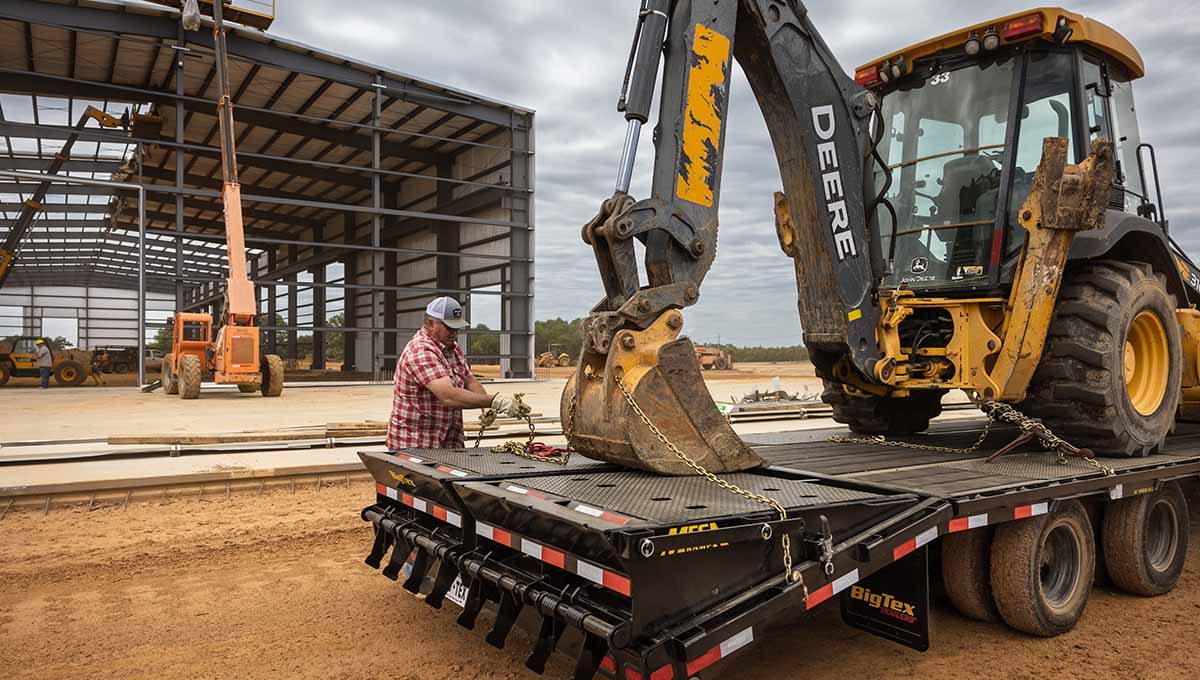 Man Wrapping Chains on Construction Equipment on Flatbed Trailer