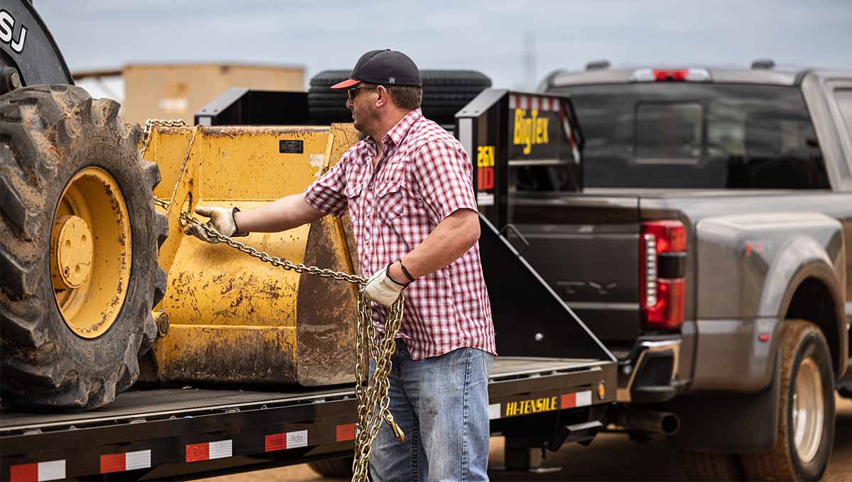 Man Wrapping Chains on Construction Equipment on Flatbed Gooseneck Trailer